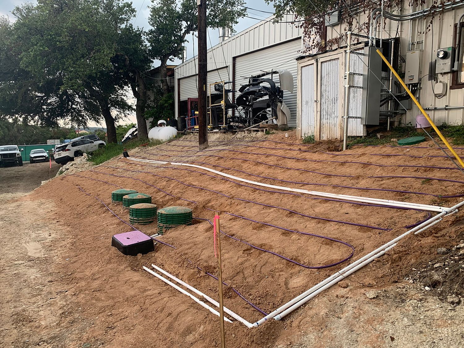 A side yard with a newly installed septic drain field featuring dark irrigation tubing laid over sandy, graded soil.