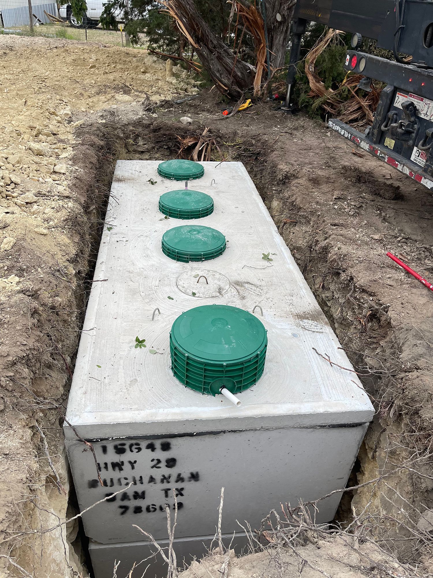 A concrete septic tank with four green access lids sits in an open trench in a rural, dirt-covered area.