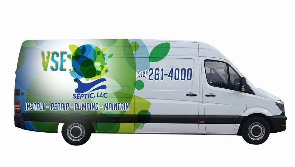 A service technician crouches over an open septic tank, using a large green suction hose to pump out the contents.