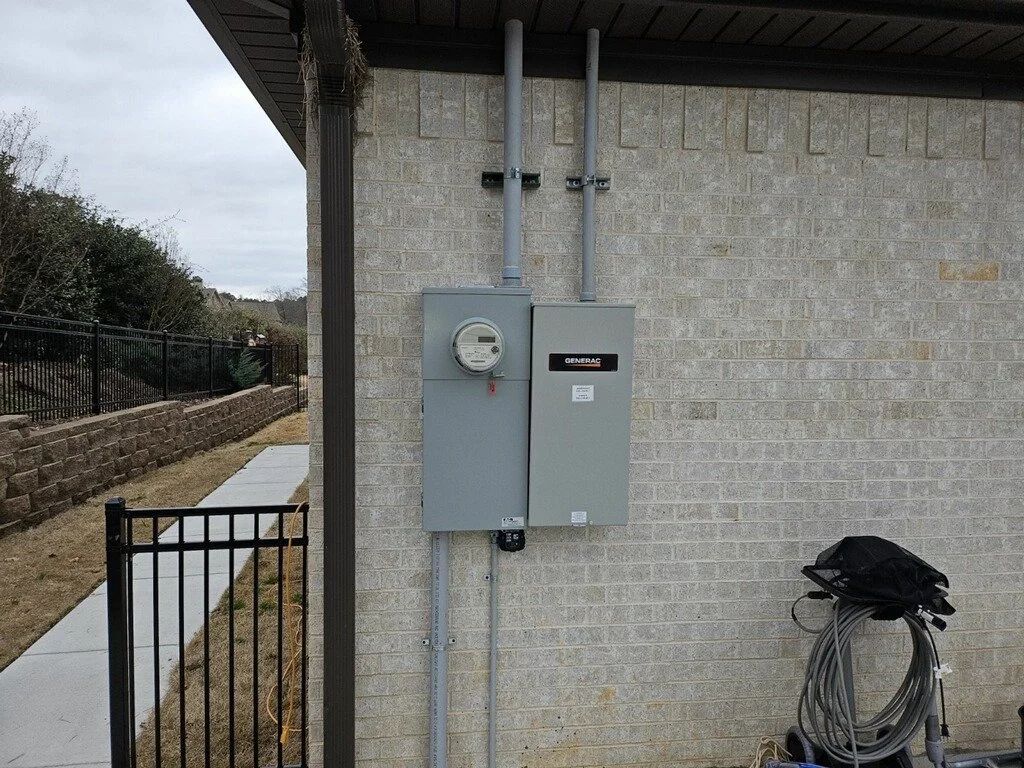 Outdoor utility meters and electrical boxes mounted on a stone wall beside a walkway.