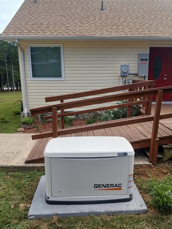 White Generac backup generator on a concrete pad beside a house and wooden accessibility ramp.