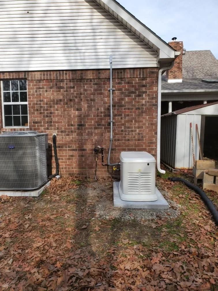 Backyard view of a brick house wall with an outdoor air conditioner unit and fallen leaves.