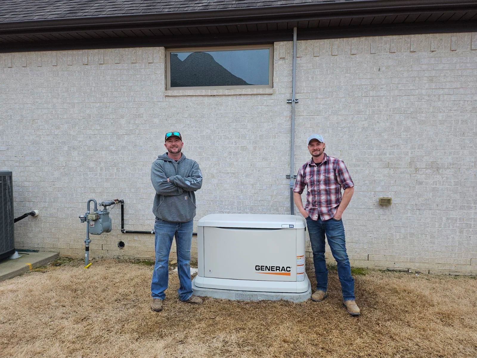 Two men stand beside a large white tank against a gray building wall.