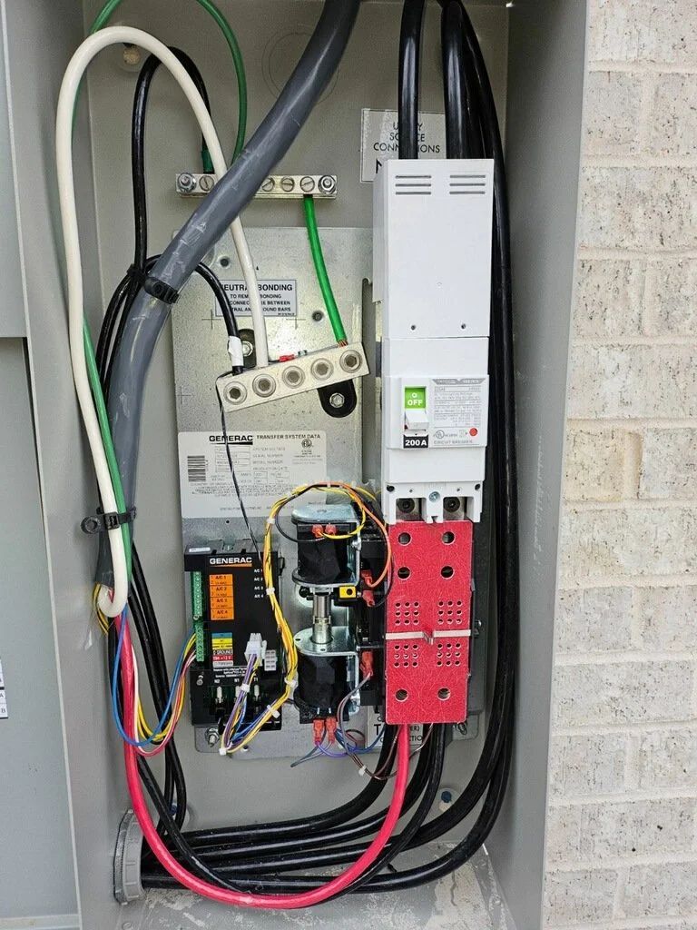 Open electrical control panel with red wiring, white modules, and black cables mounted on a cinder block wall