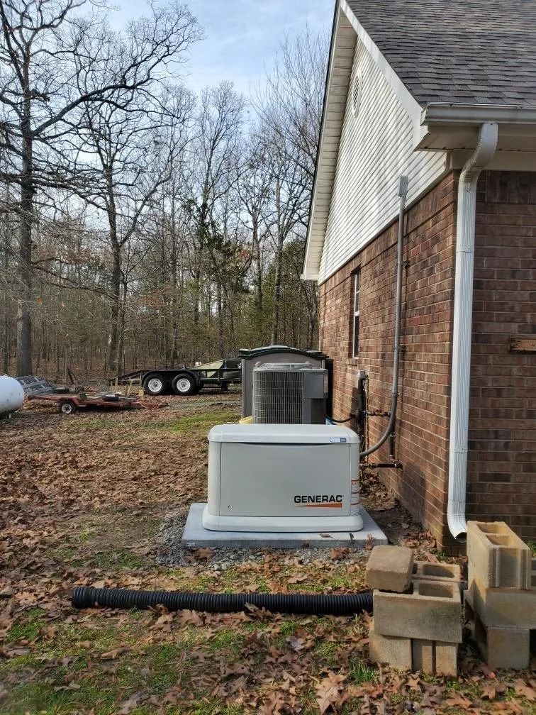 Outdoor HVAC unit beside a brick house with a gutter downspout and wooded yard behind it