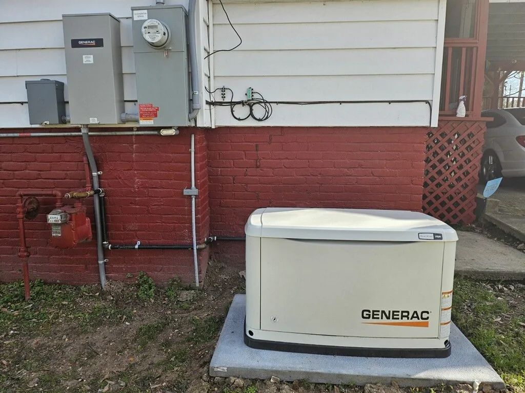 Generac generator beside a house, next to utility meters and red brick siding