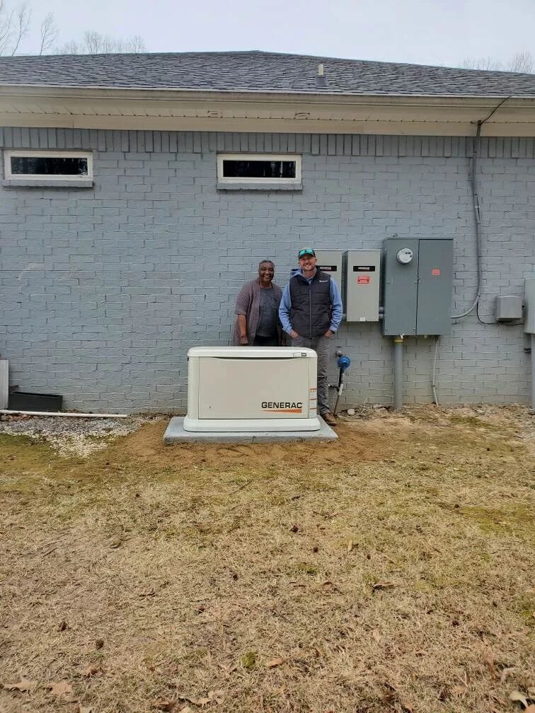 Two workers stand beside an outdoor HVAC unit against a gray brick building.