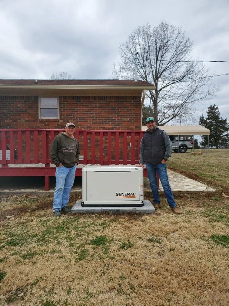 Two people standing beside a white generator in front of a brick house on an overcast day