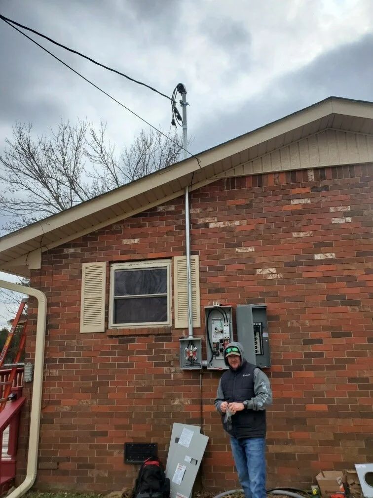 Worker standing beside house electrical meter on a red brick wall, wearing a hard hat and vest