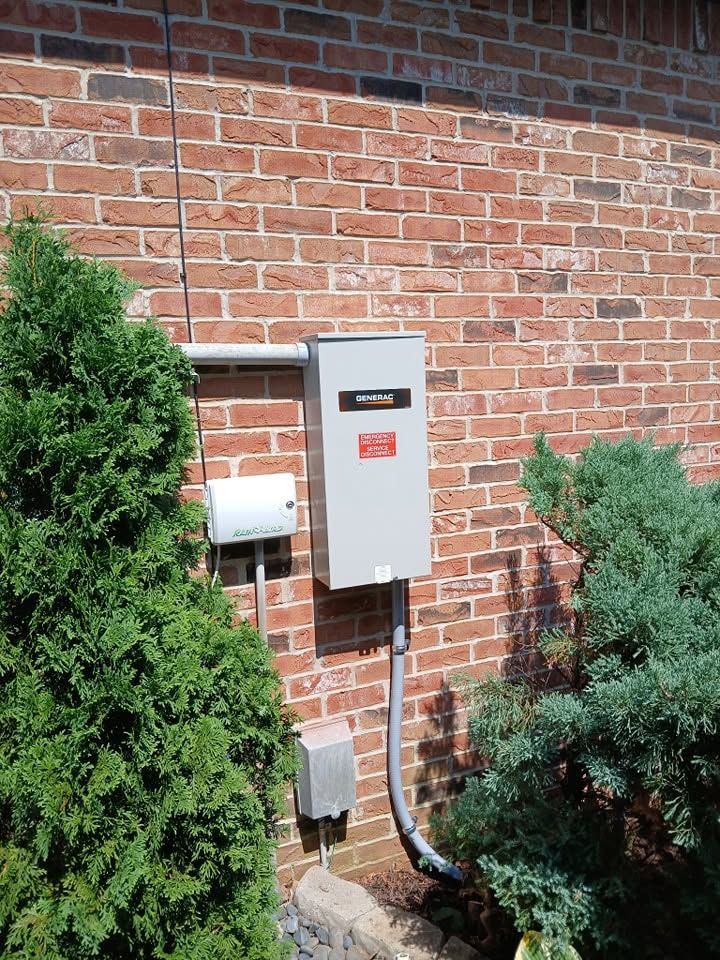 Outdoor electrical panel on a brick house wall with conduit and shrubbery nearby