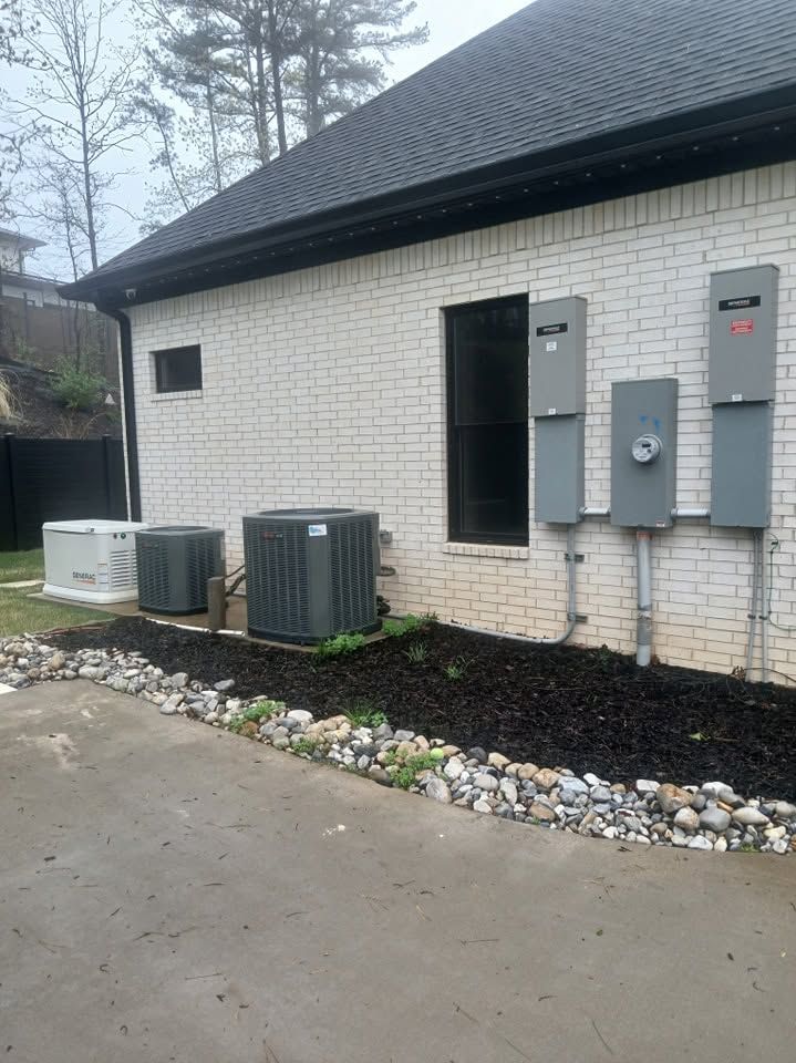 Side of a white brick building with utility meters, HVAC units, and a gravel border beside a wet driveway