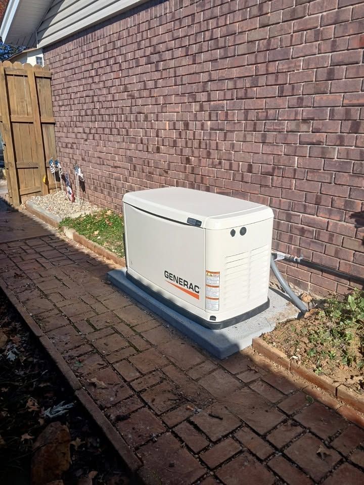 White generator unit on a concrete pad beside a brick wall and wooden fence in a backyard.