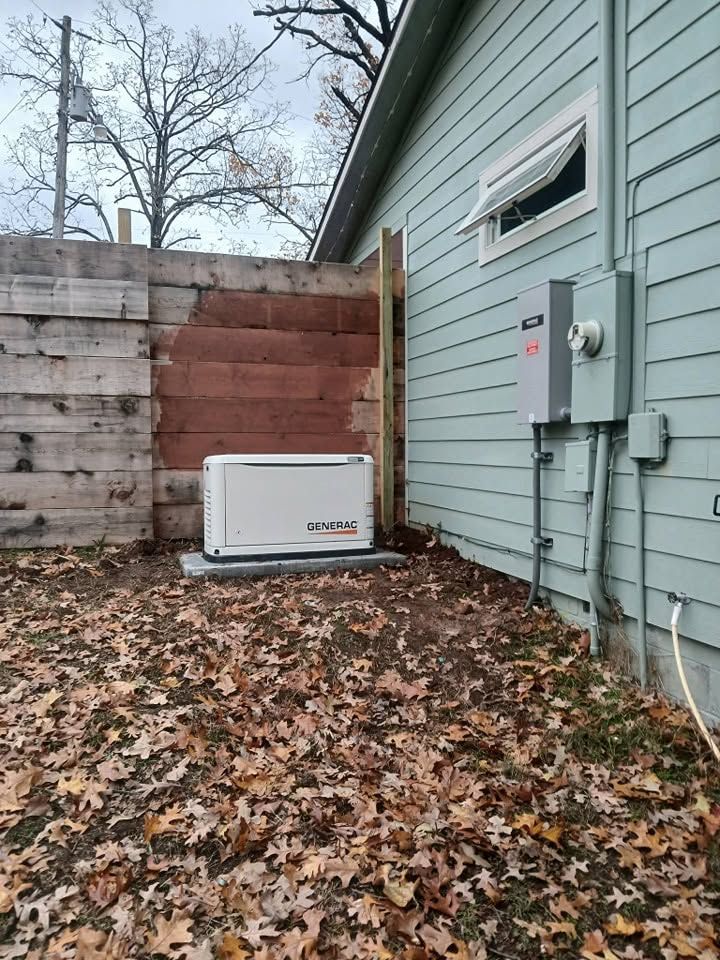 Outdoor generator beside a house, with gray siding, brick wall, and fallen leaves on the ground
