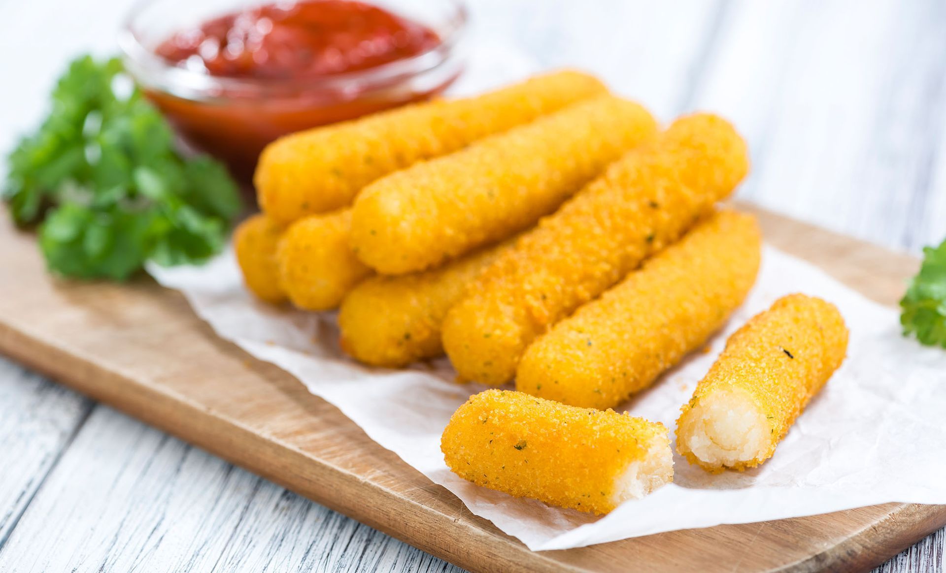 Fried mozzarella sticks on a wooden cutting board with ketchup.