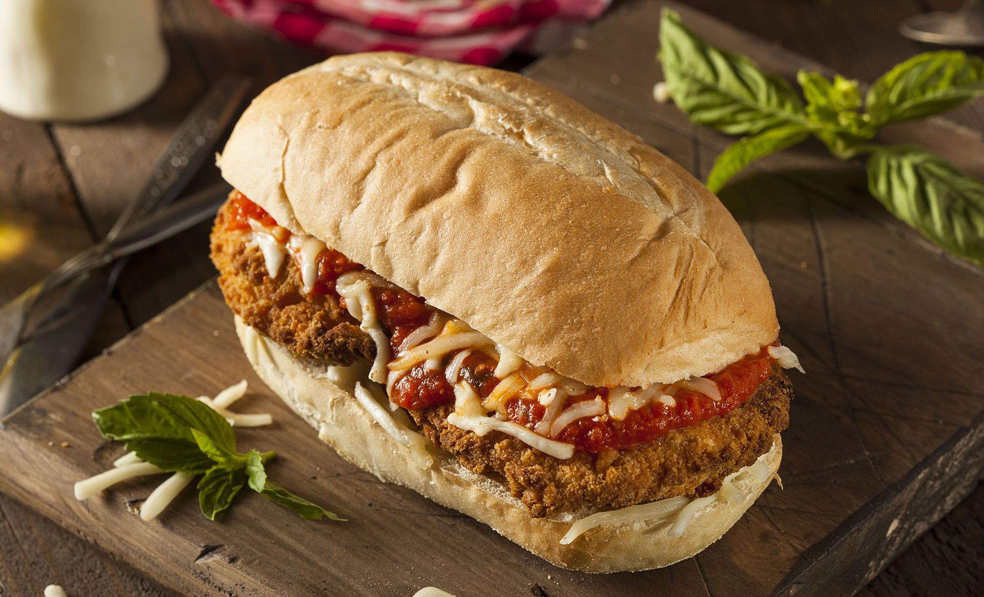 A chicken parmesan sandwich is sitting on a wooden cutting board.
