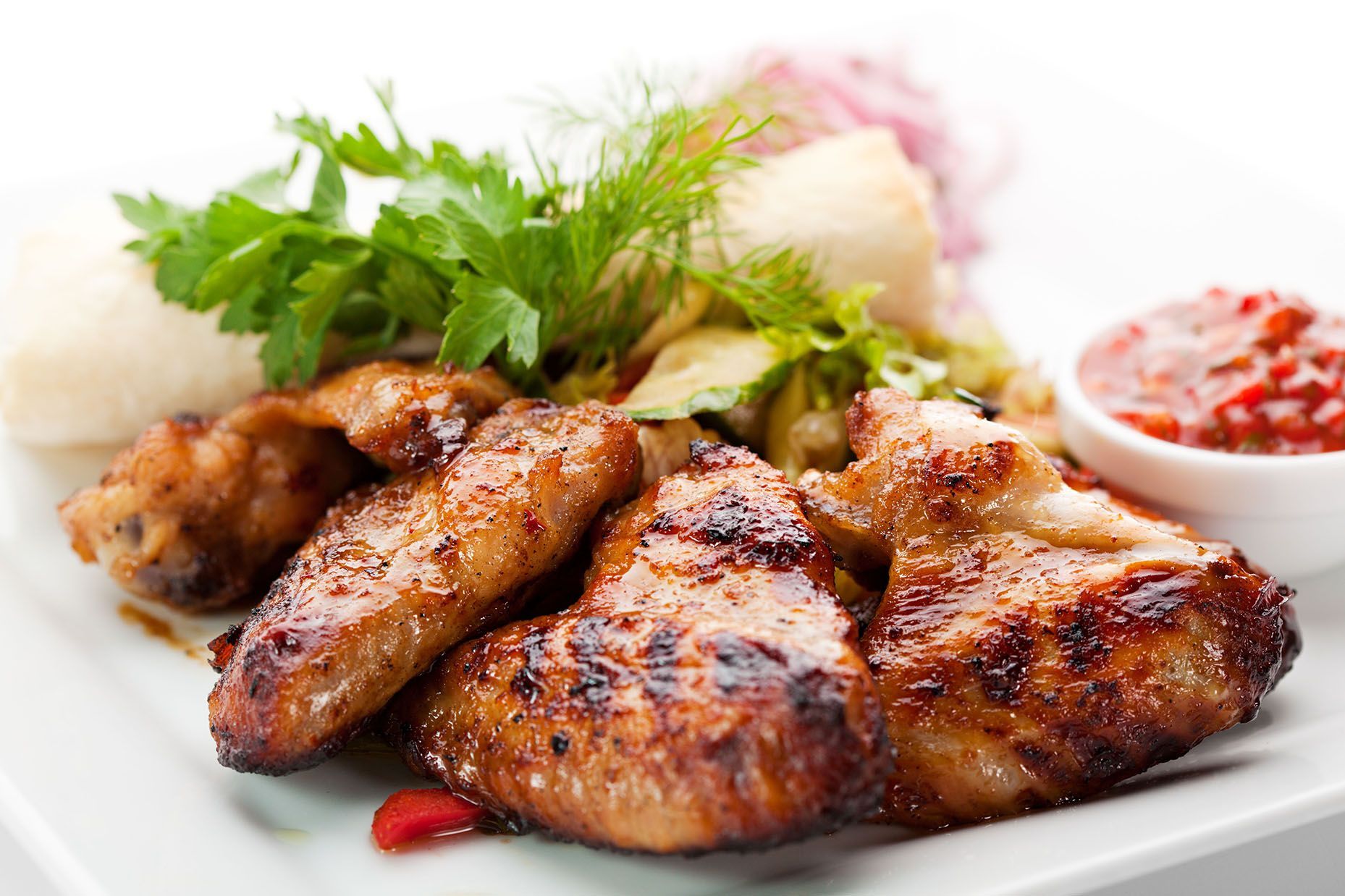 A white plate topped with grilled chicken wings and vegetables.