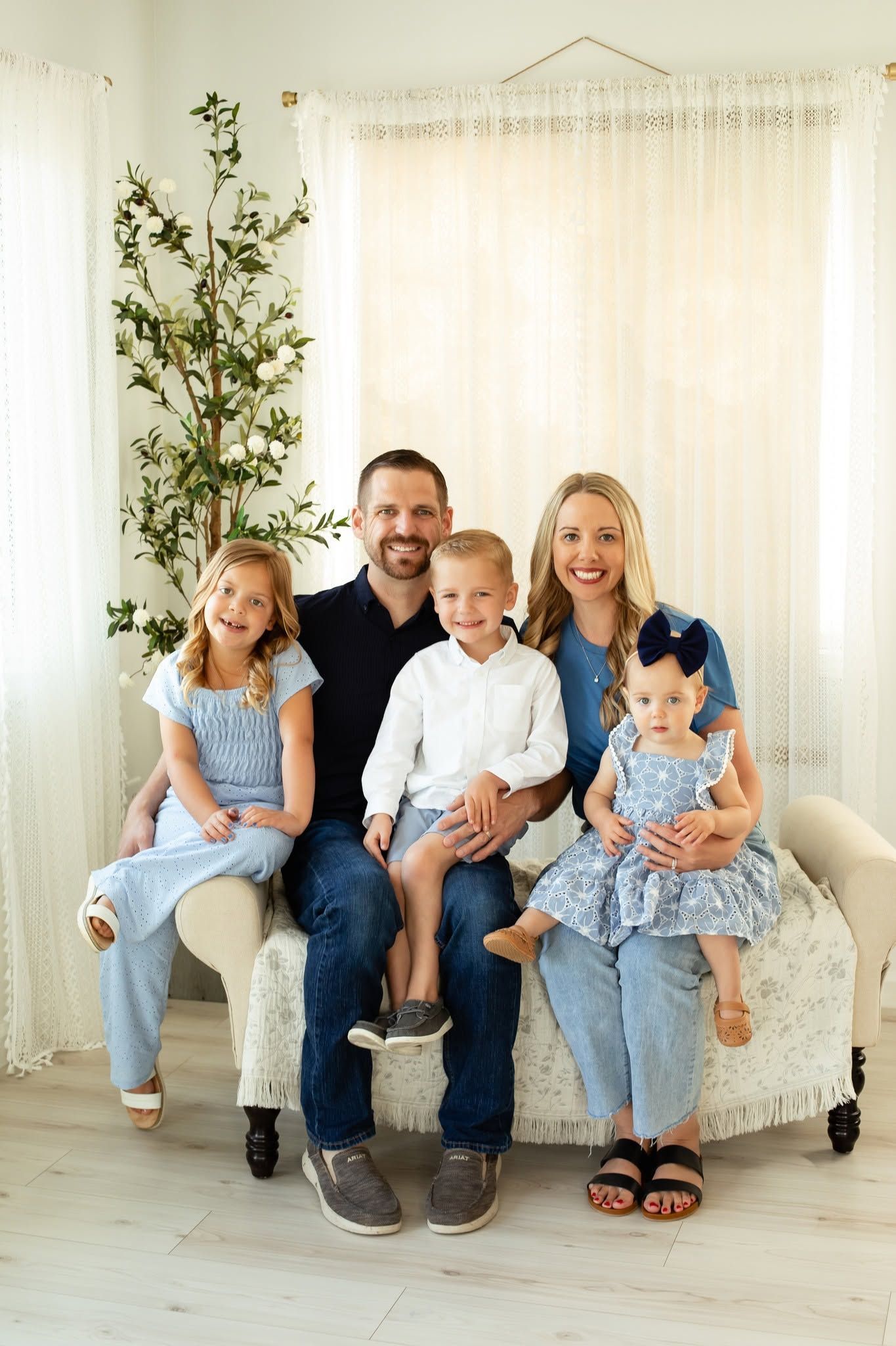 Family seated on a white couch in a bright room, smiling at the camera.