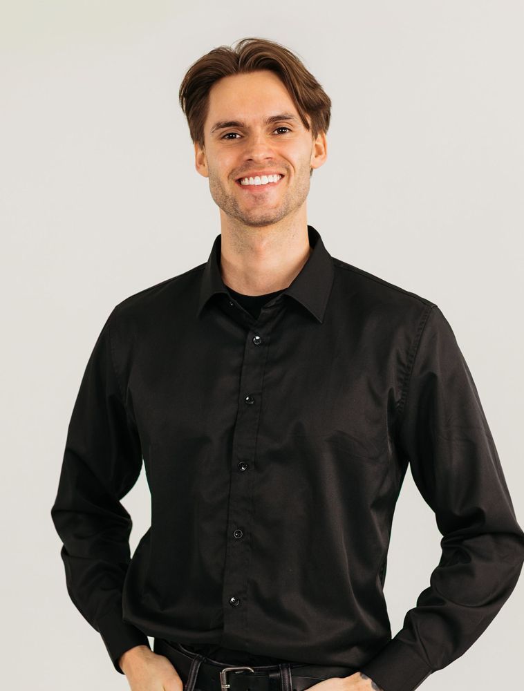 Smiling person in a black shirt standing against a light background.