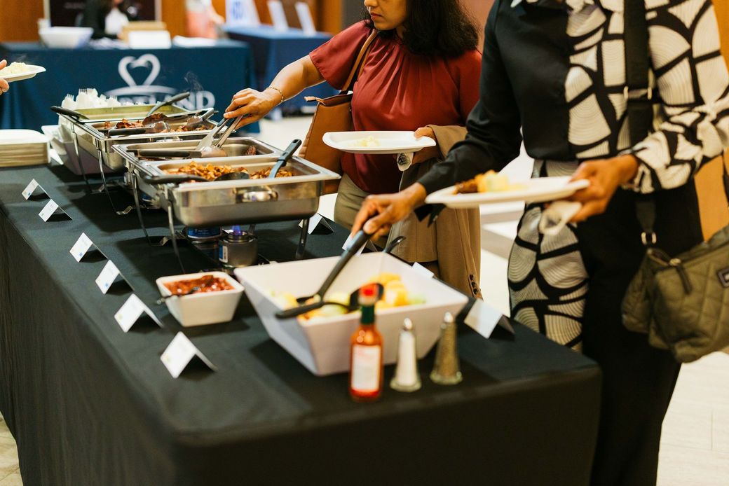 Buffet table with salad bar, pasta, cherry tomatoes, and orange dressing in white serving dishes.