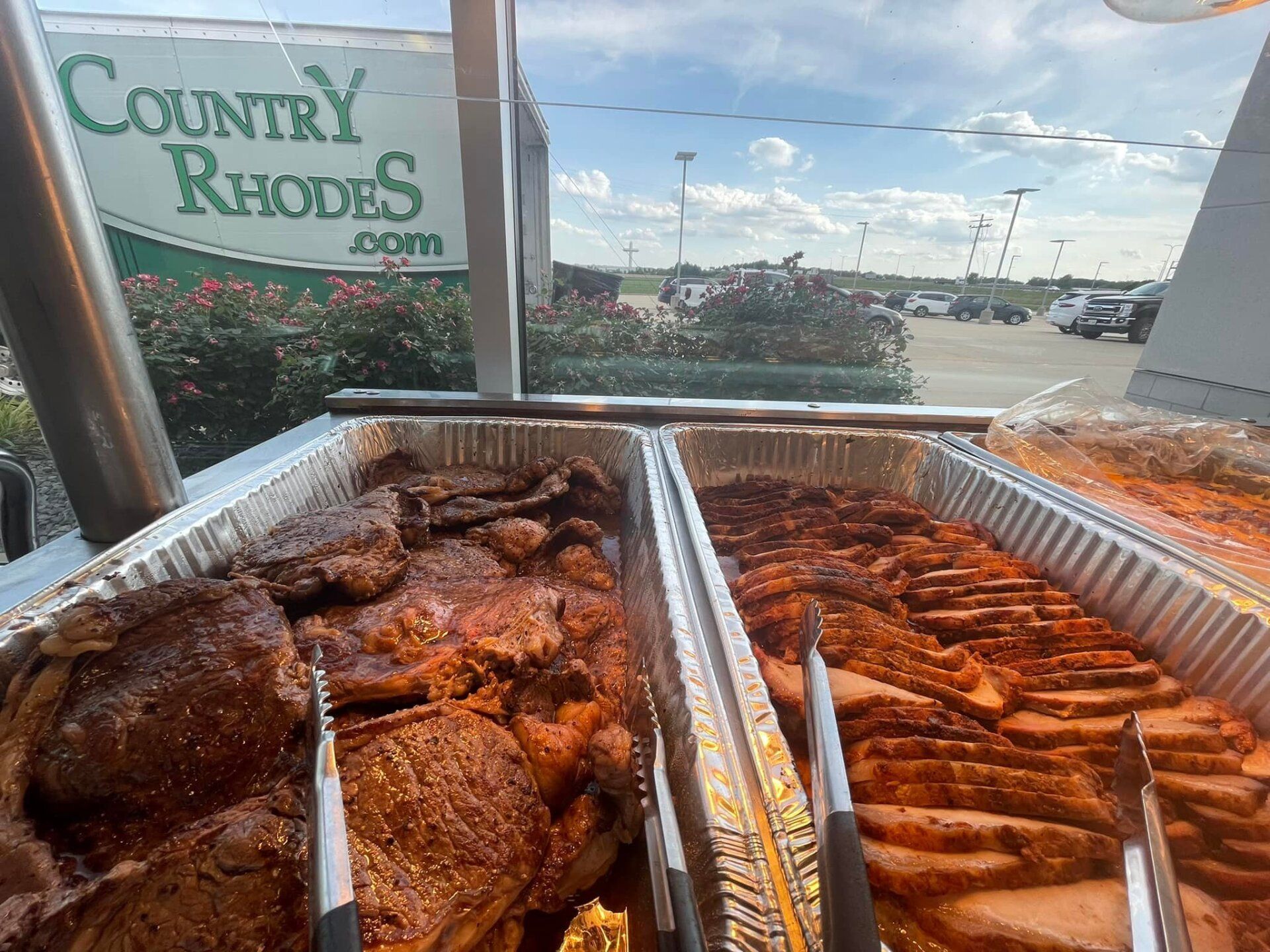 Trays of roasted meat at Country Rhodes market stall by a roadside window