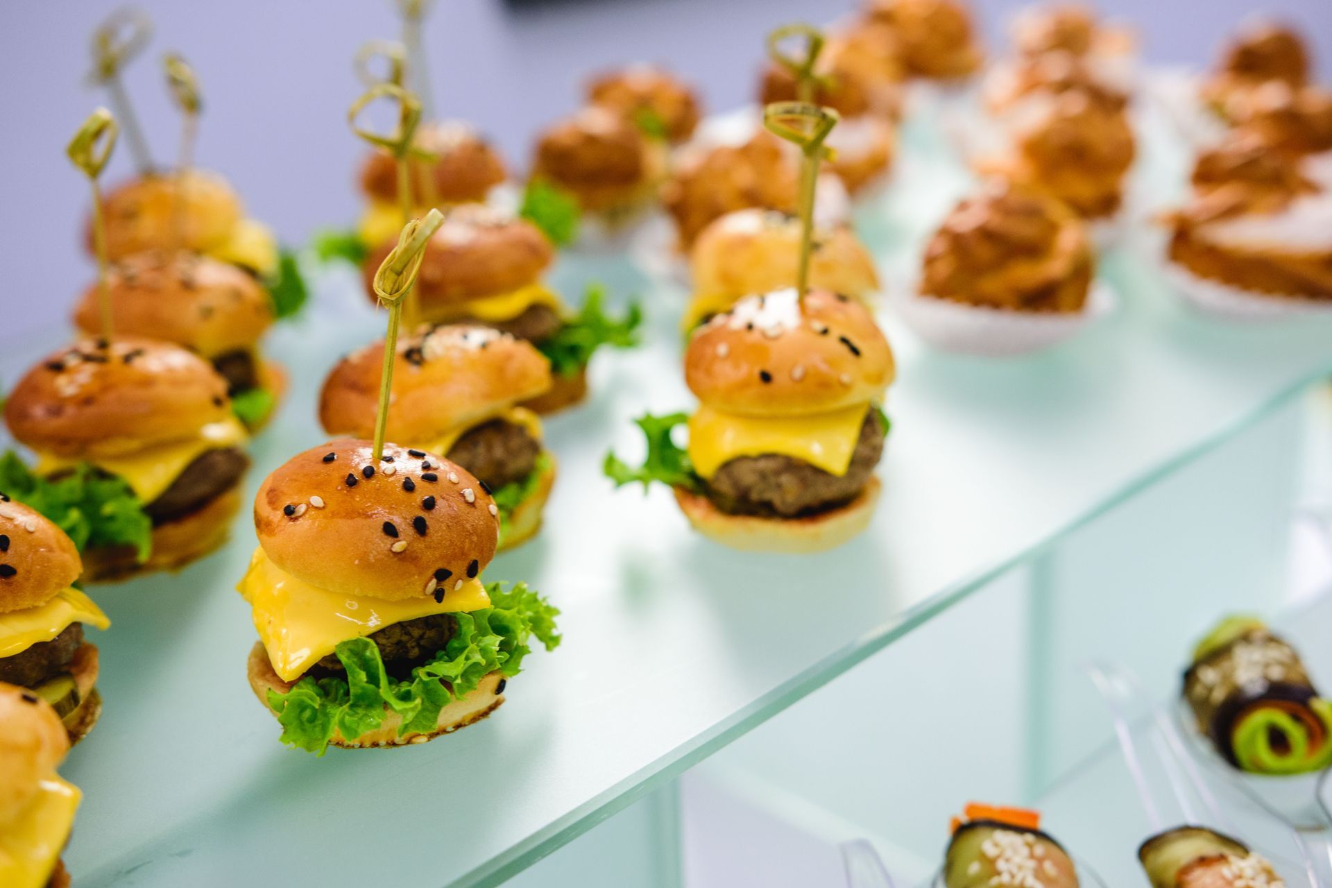 Mini burgers on skewers arranged on a glass tray at a catered event