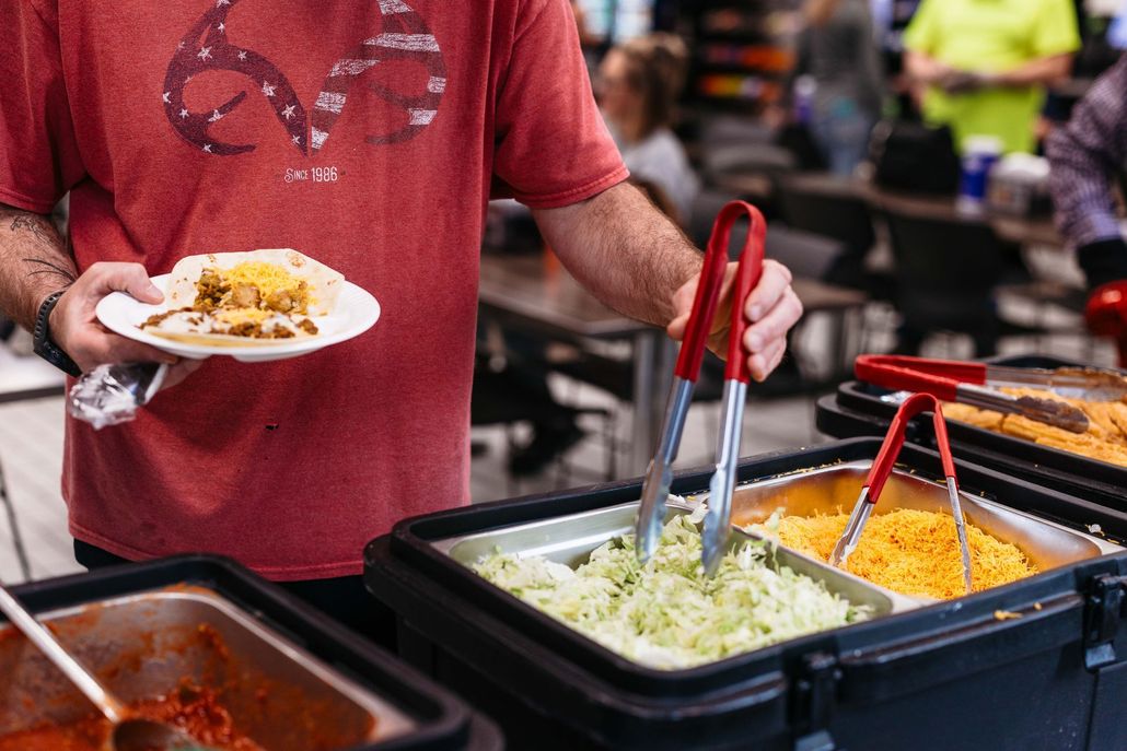 Person serving food from buffet trays onto a plate in a casual dining setting