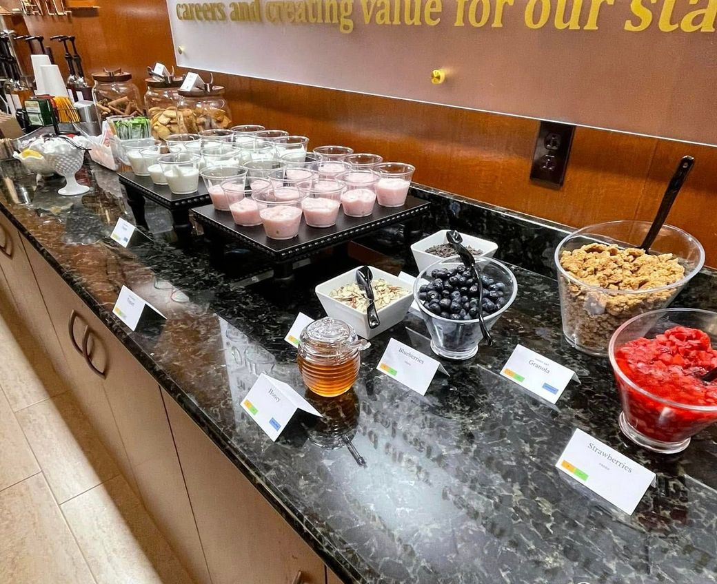 Buffet dessert display with yogurt cups, berries, granola, and honey on a marble counter.