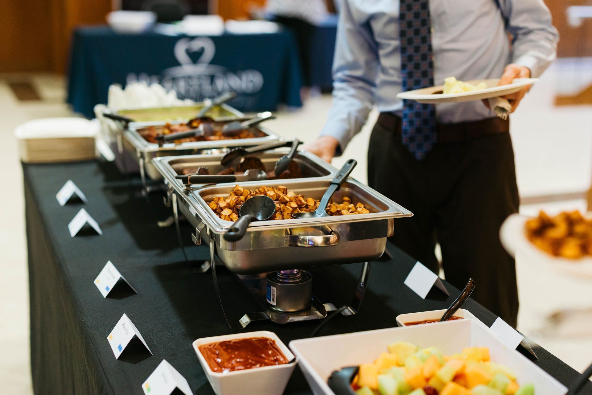 Buffet table with chafing dishes and a server holding a plate of food