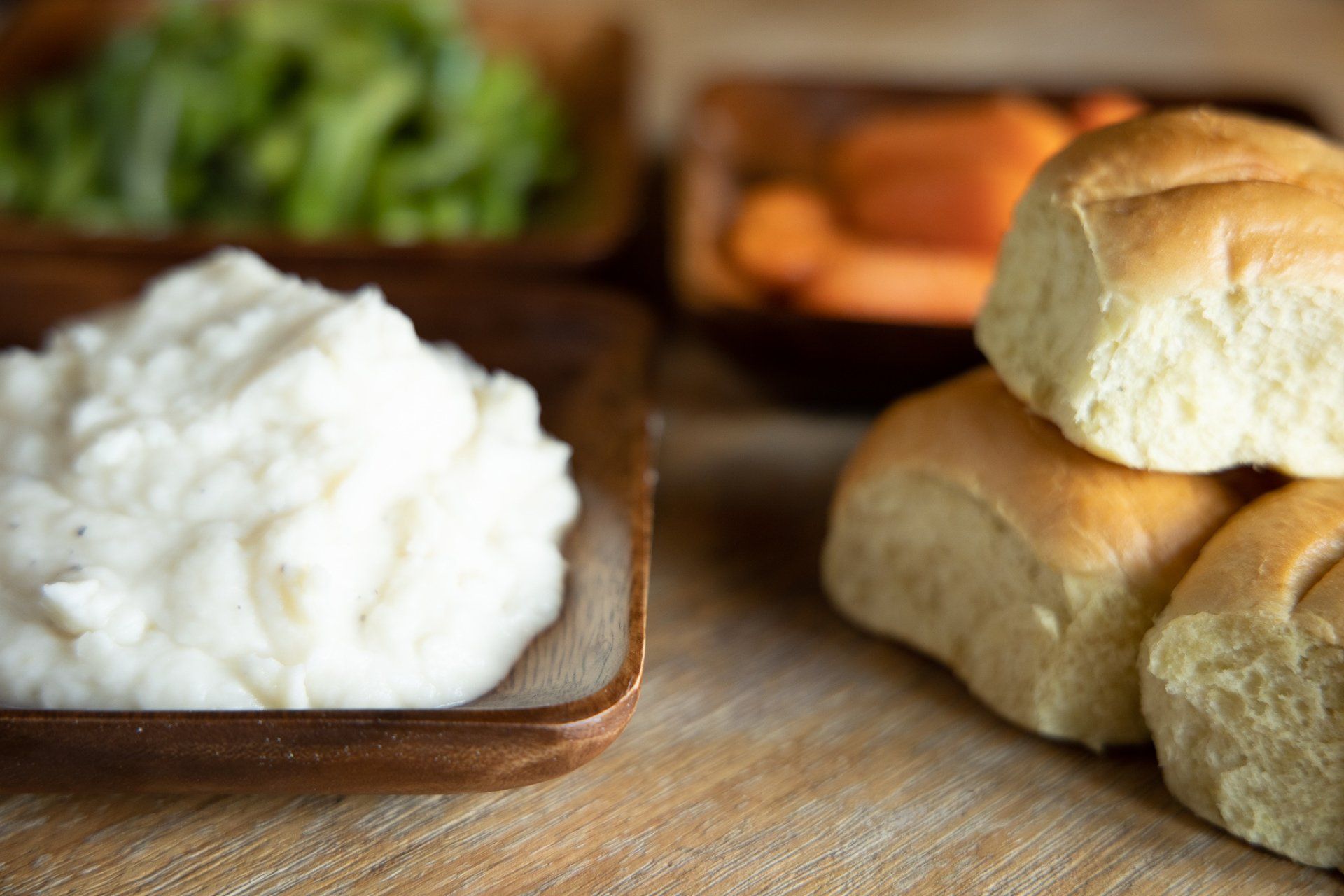 Biscuits and a bowl of whipped cream on a wooden table with blurred food in the background