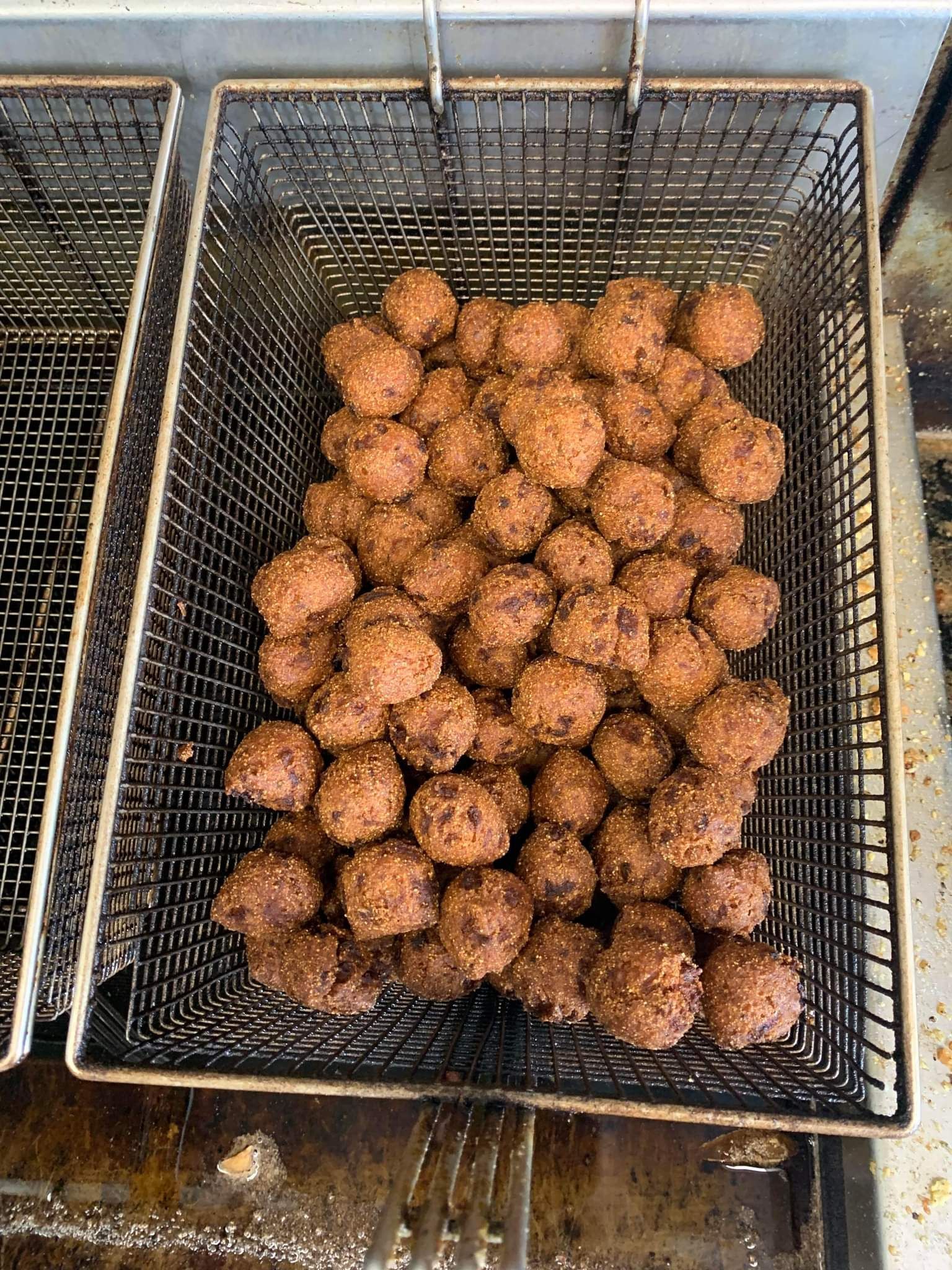 Basket of golden-brown fried fritters draining in oil inside a wire fryer basket.