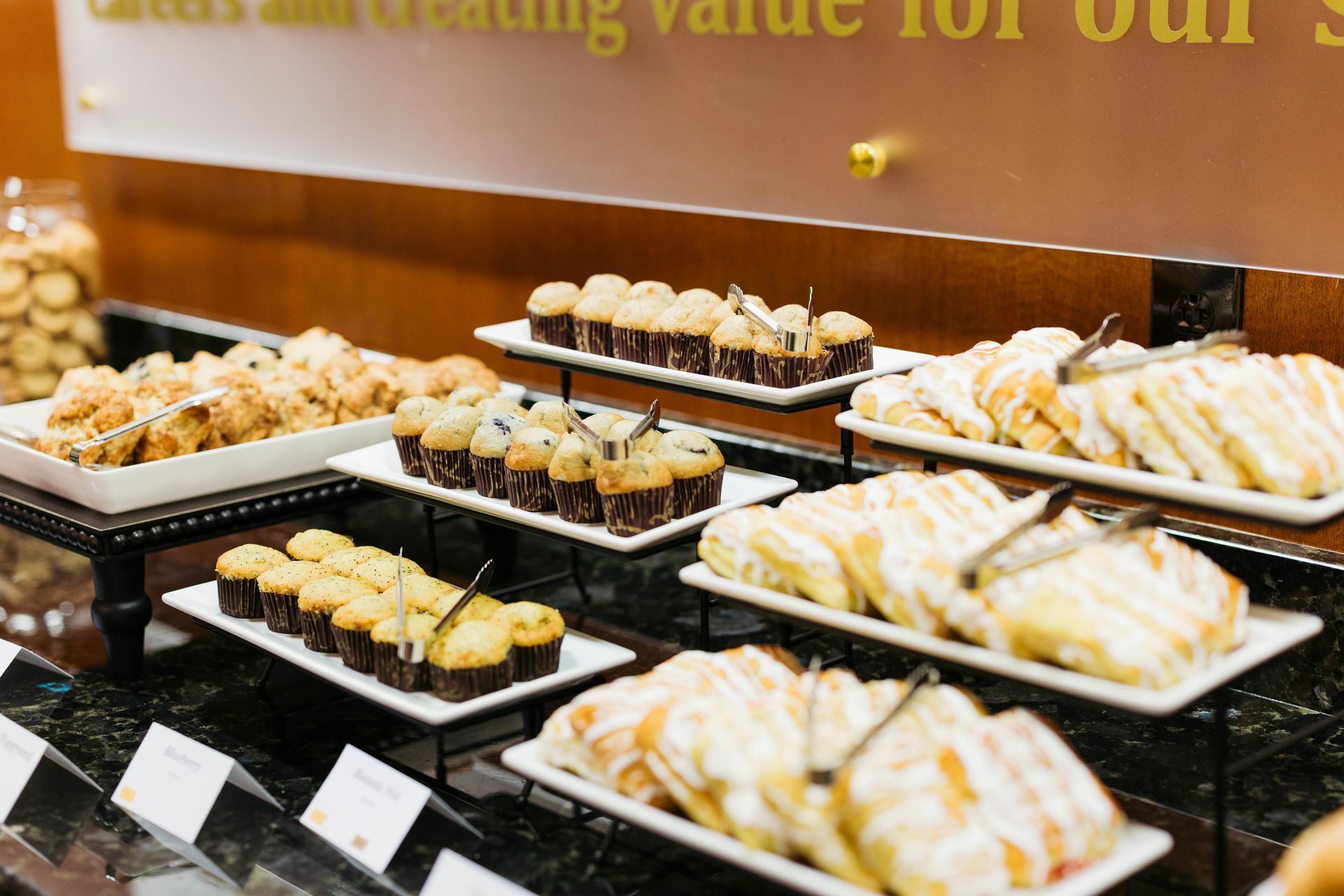 Assorted pastries on black trays displayed on a bakery counter with small labels