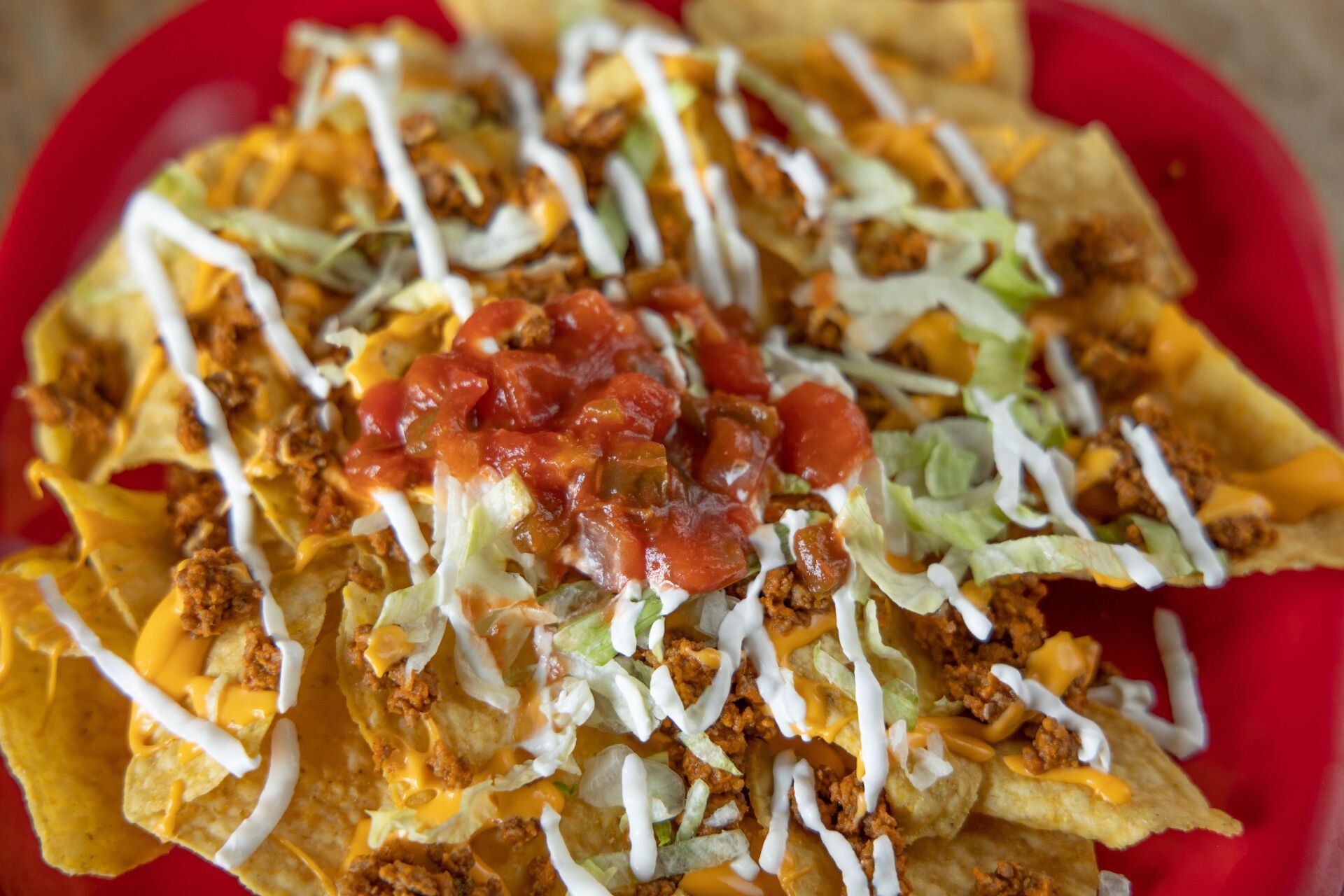 Loaded nachos with shredded lettuce, cheese, salsa, and sauce on a red plate.