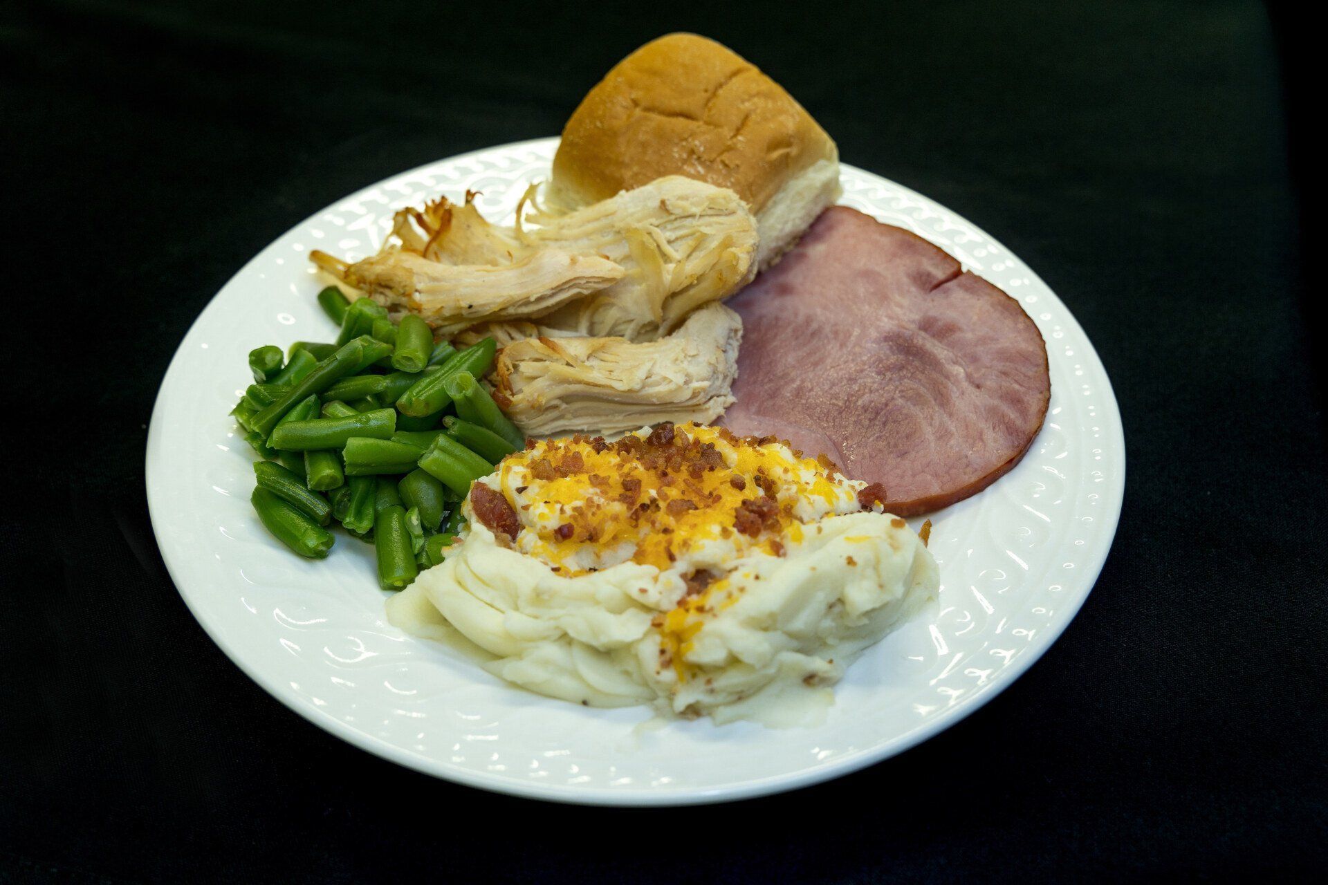 Plate with sliced ham, green beans, bread, and a cheesy egg dish on a white plate