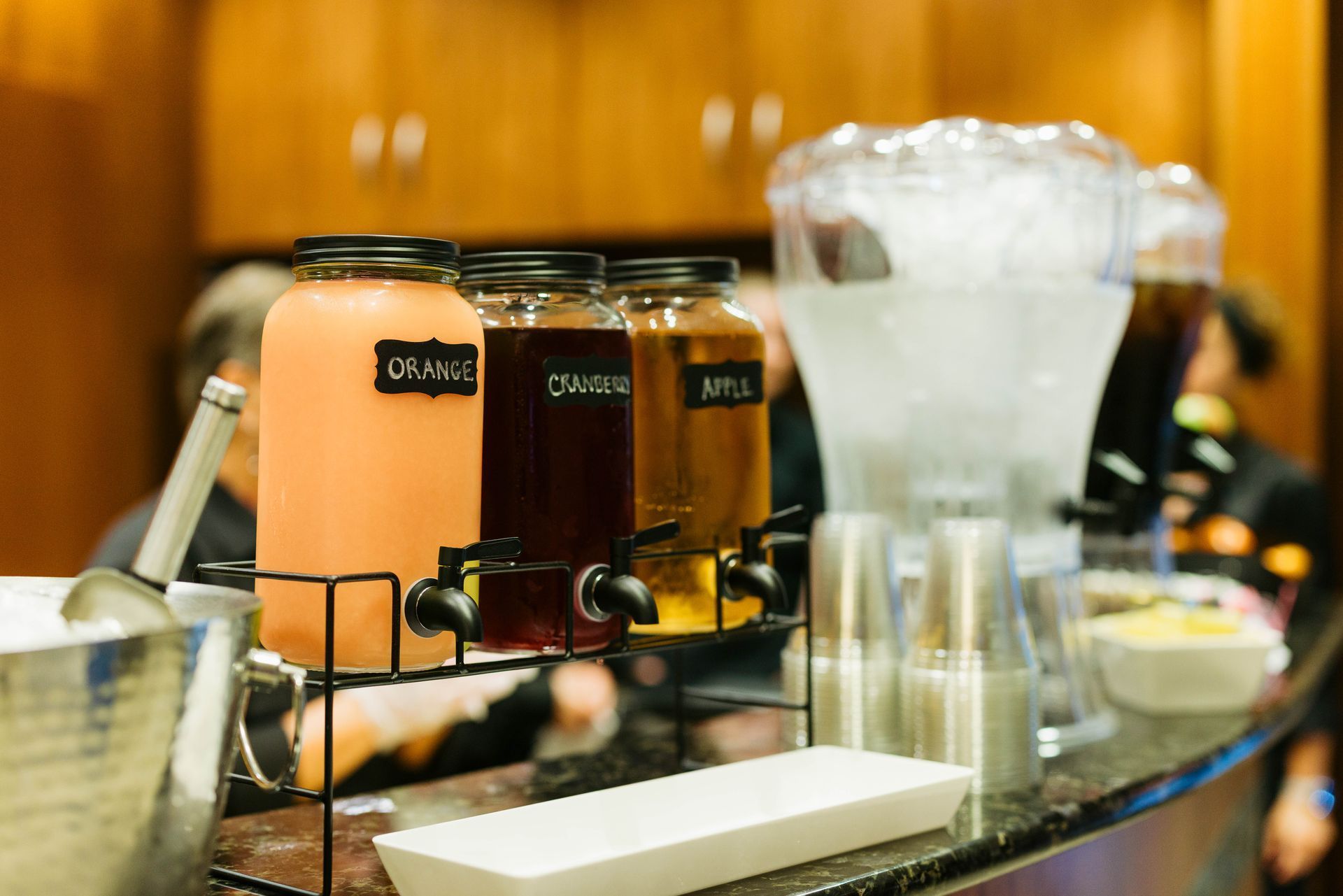 Buffet beverage dispensers with orange juice and milk on a counter, with cups and a pitcher nearby