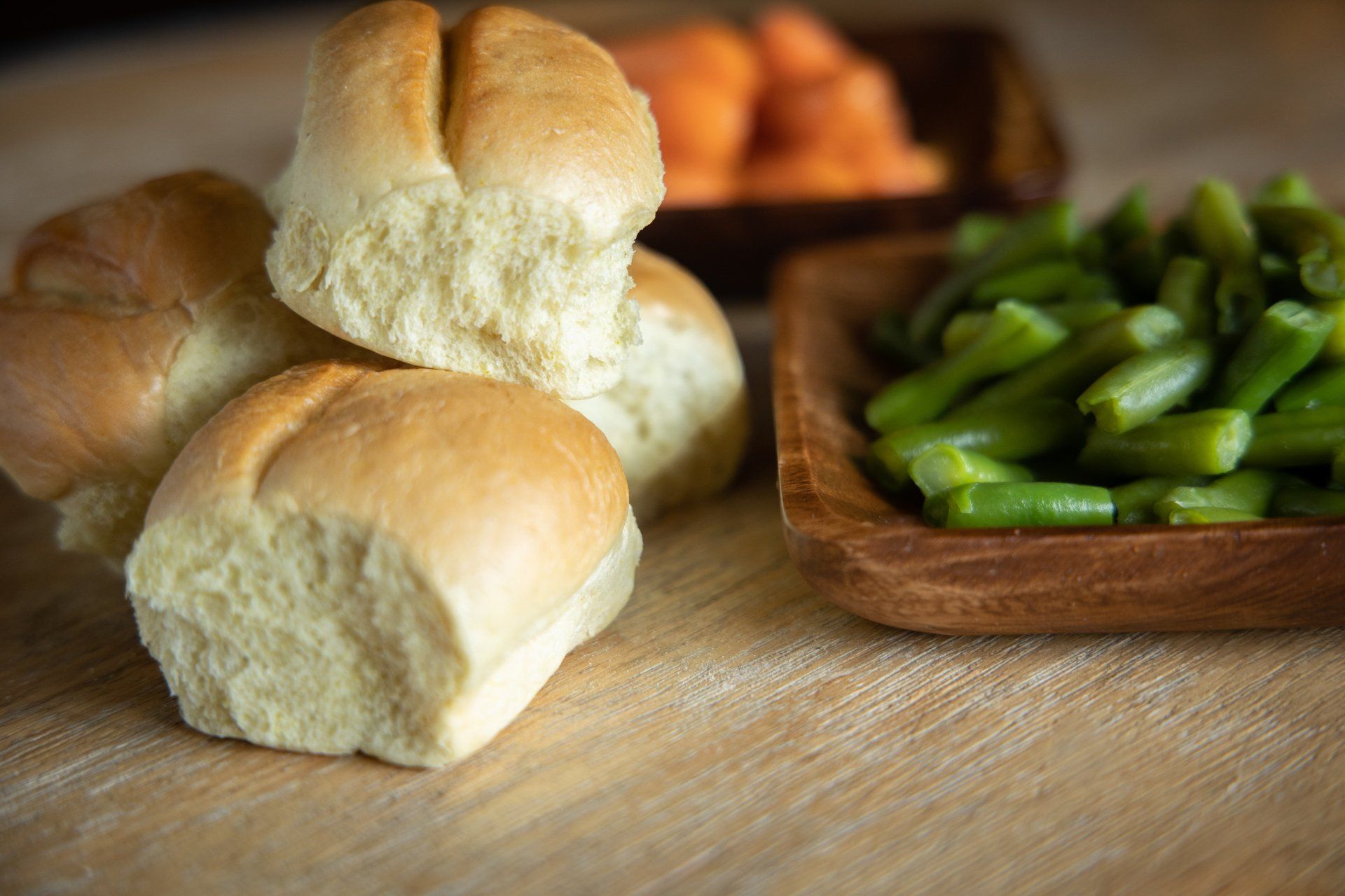 Fresh bread rolls beside a wooden bowl of green asparagus on a table