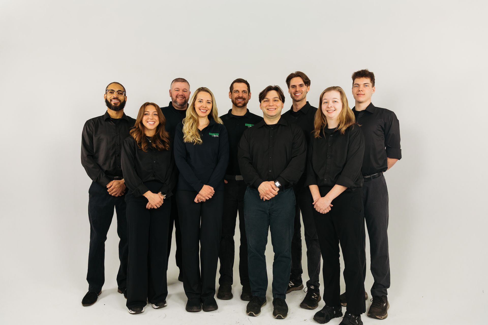 Group of eight people standing together in black outfits against a plain white background.