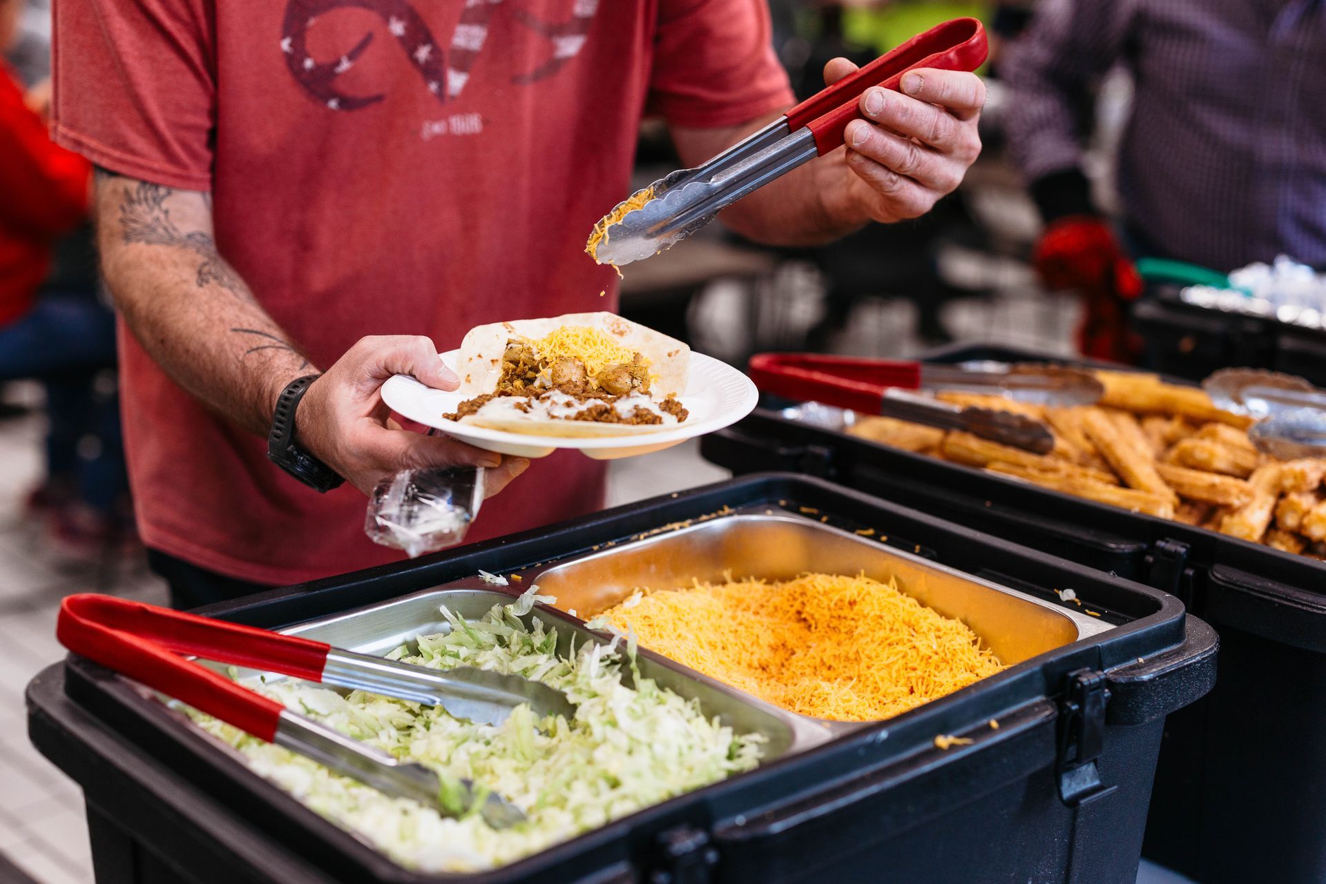 Person serving food at a buffet with tongs, next to trays of rice and dishes