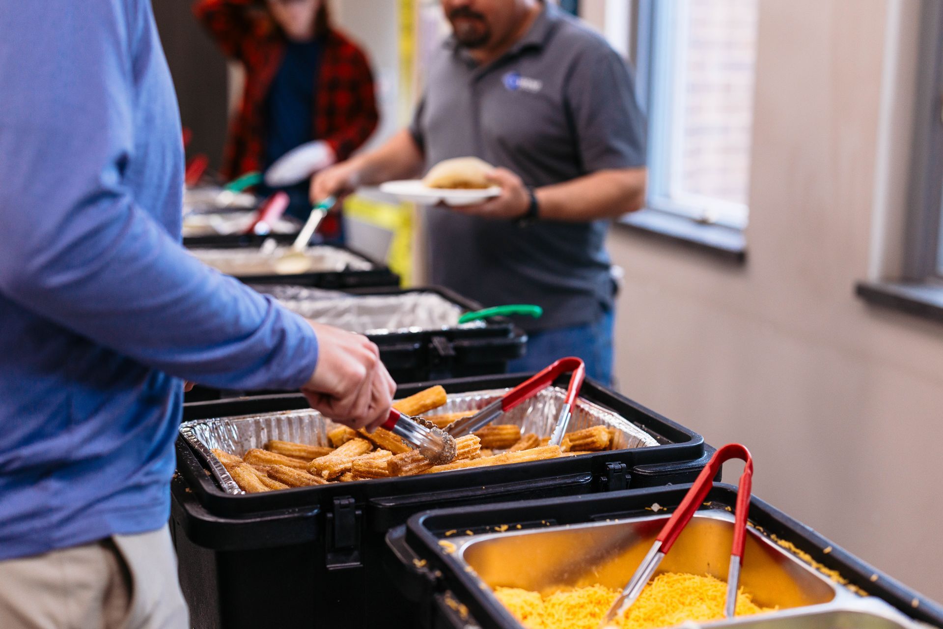 People serving food from buffet pans with tongs at a catered indoor event