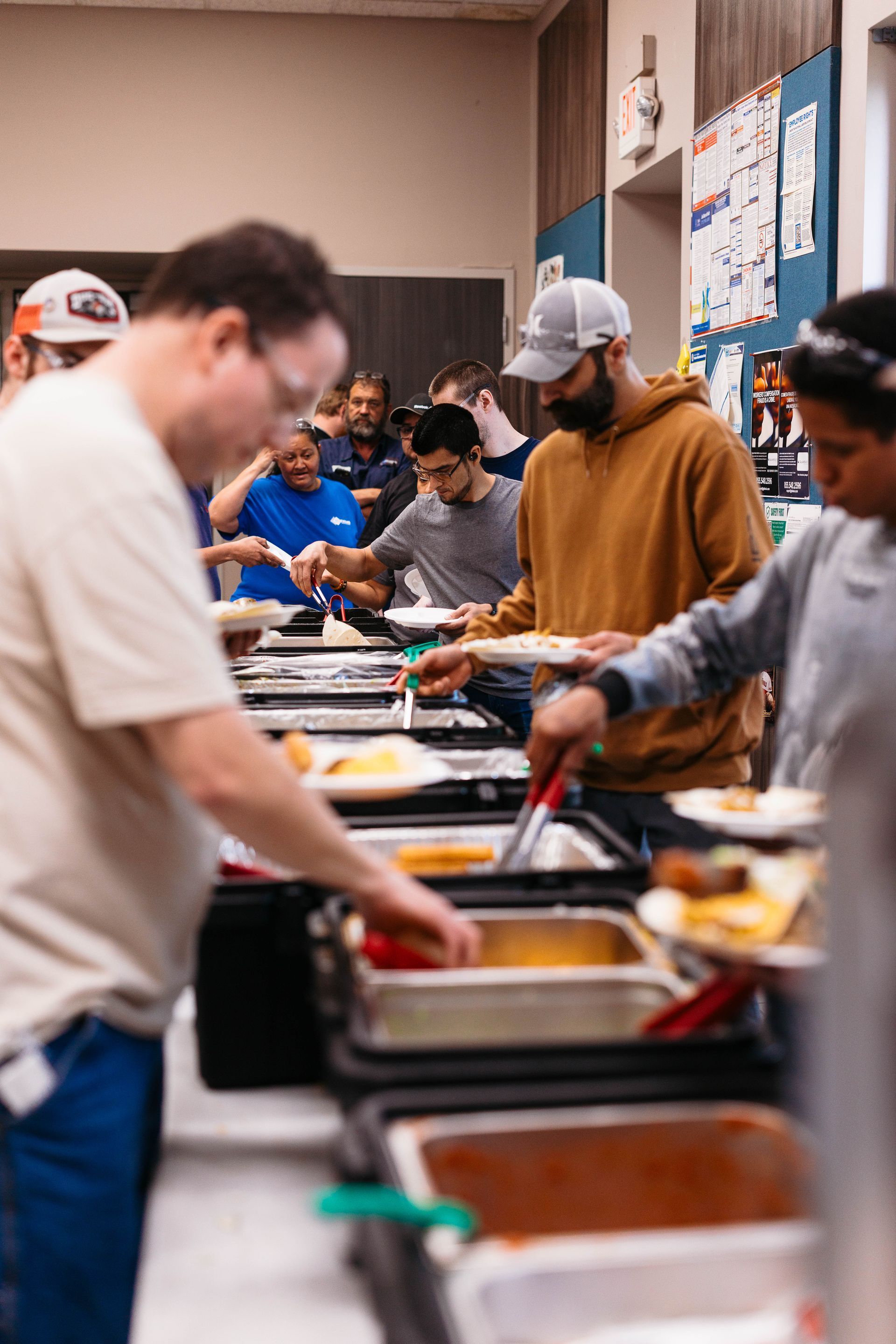 People serving themselves at a cafeteria buffet with food trays and condiments