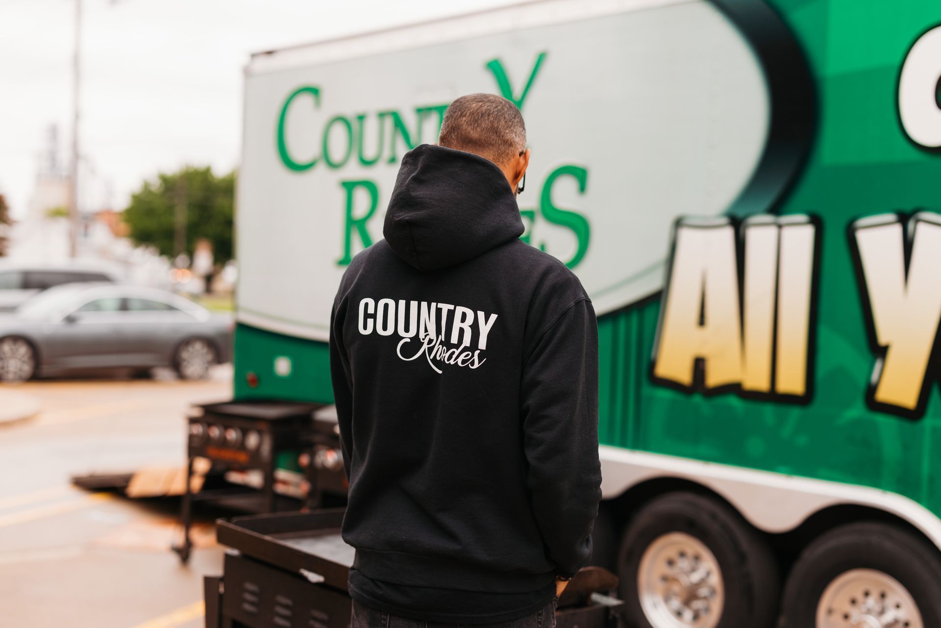 Person in black Country Cross shirt standing beside a green-and-white Country Cross trailer.
