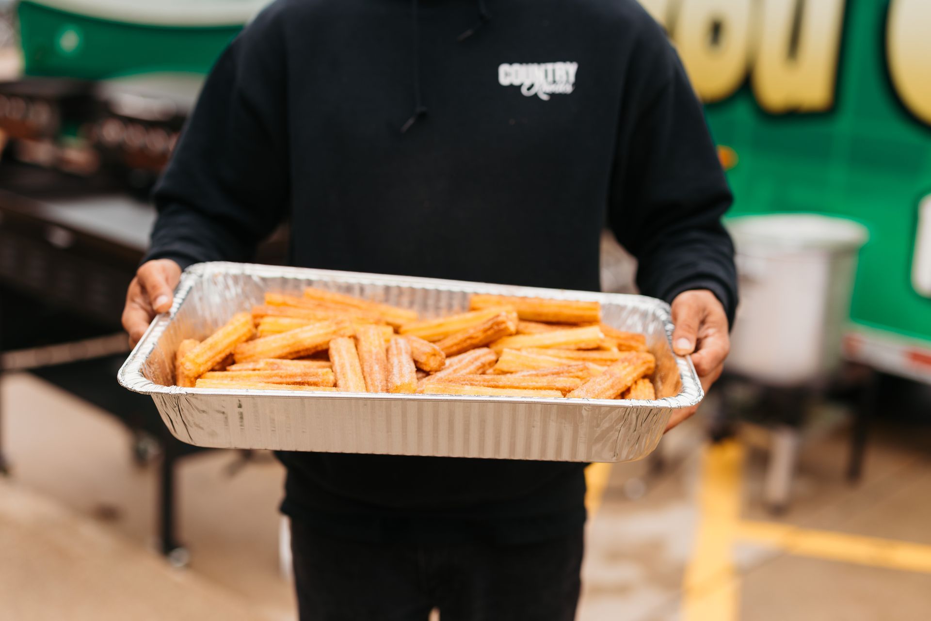 Person holding a tray of orange fried snacks in a food stall.