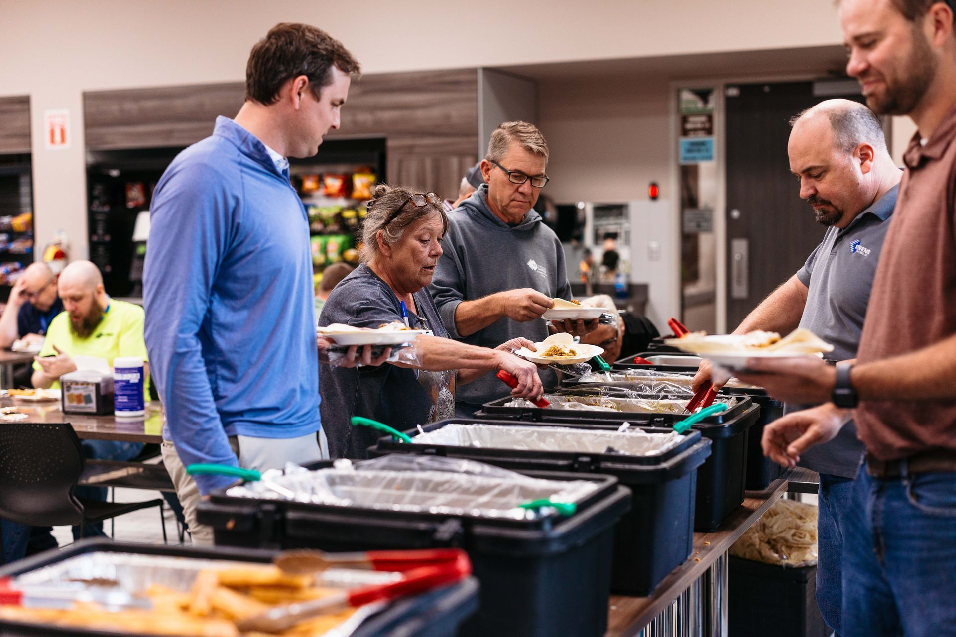 People serving food at a buffet table in a busy dining hall