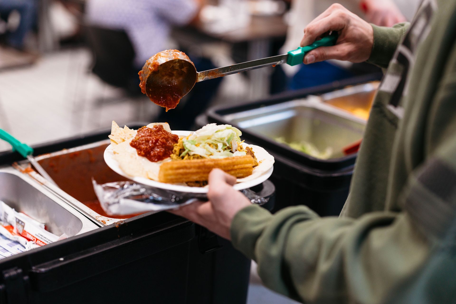 Person serving food from a buffet tray onto a plate with mashed potatoes and meatballs