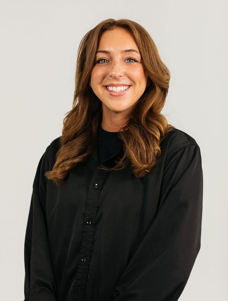 Smiling person with brown hair wearing a black shirt against a light background
