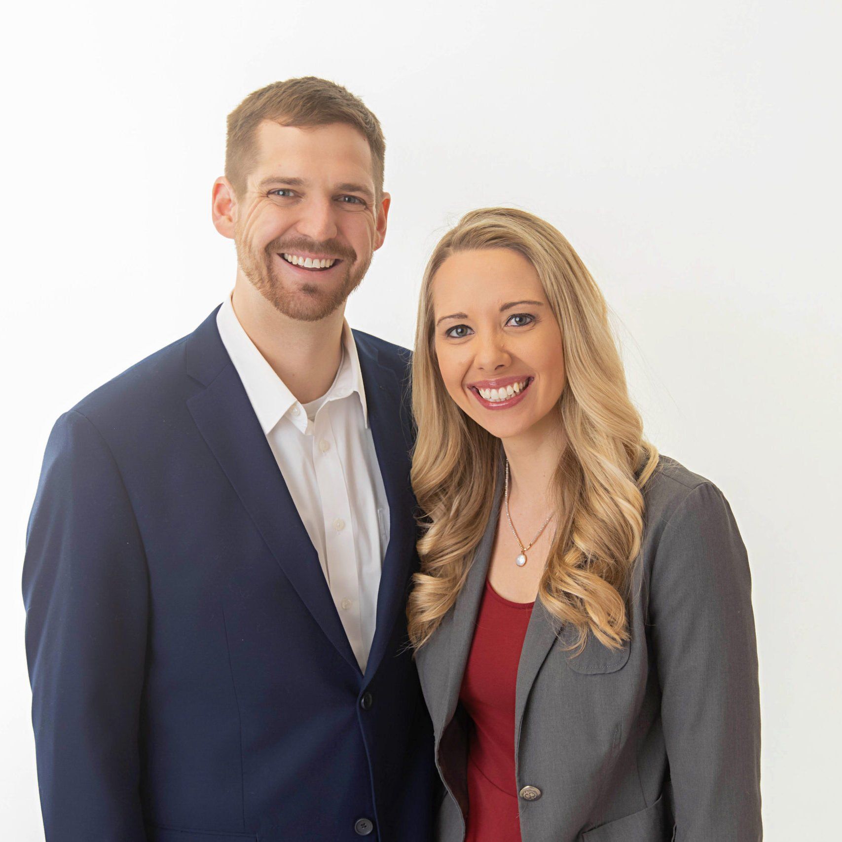 Two smiling professionals standing side by side against a light background