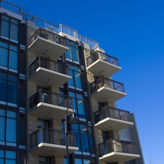 A modern multi-story apartment building with stacked balconies against a clear blue sky.