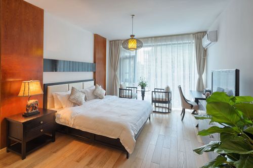 A modern bedroom featuring a bed with white linens, a dark nightstand, a desk with a chair, and a potted plant.