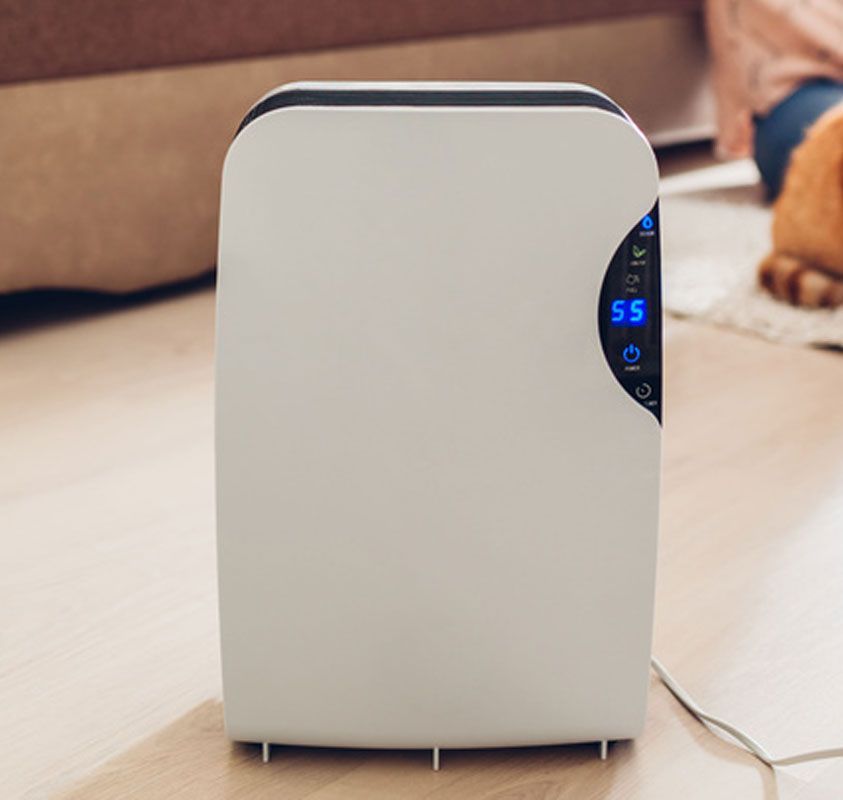 White air purifier with blue digital display on a wooden floor in a living room