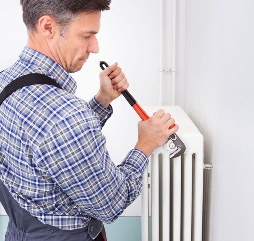 Man tightening a white radiator valve with a wrench in a bright room