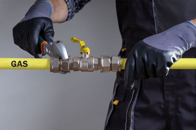 Worker tightening a yellow gas line valve with gloved hands